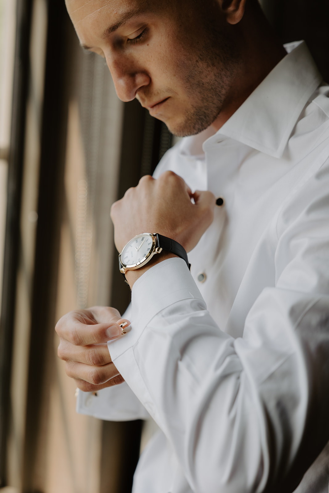 Close-up of the groom fastening his gold cufflink while getting ready for the wedding ceremony.